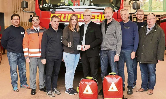 Gruppe von Personen vor Feuerwehrauto mit Notfallrucksack